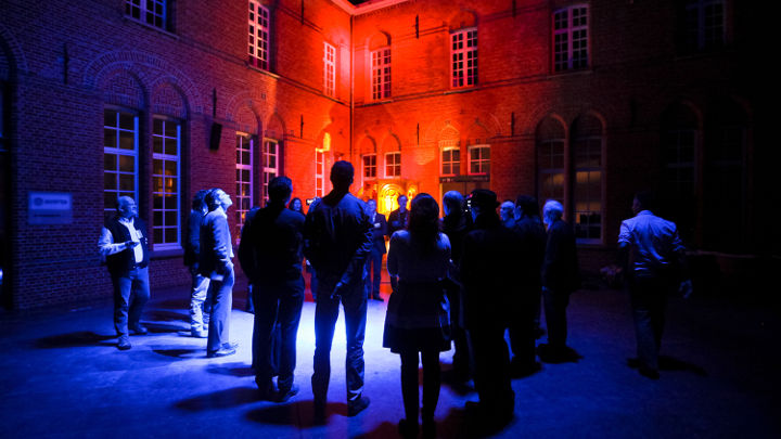 Iso ihmisryhmä, joka keskustelee kauniisti valaistun rakennuksen ulkopuolella Belgian Turnhoutissa järjestetyn Philipsin valaistustyöpajan aikana