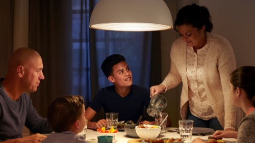 Perhe syö illallista kotona hyvin valaistun ruokapöydän äärellä