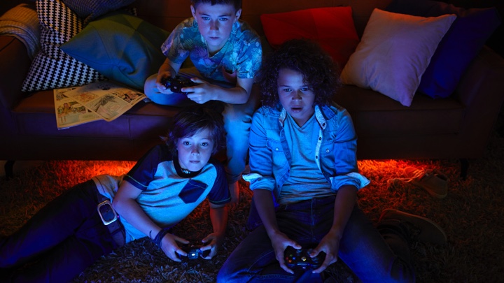 Kolme poikaa pelaamassa videopelejä tunnelmavalaistuksessa